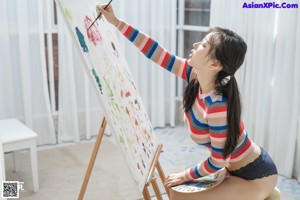 A woman sitting on a stool in front of a painting.