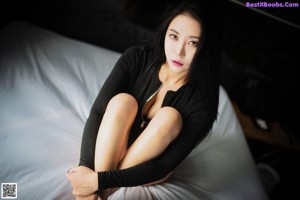 A woman in a black bodysuit sitting on a bed.