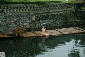 A naked woman standing on a wooden bridge.