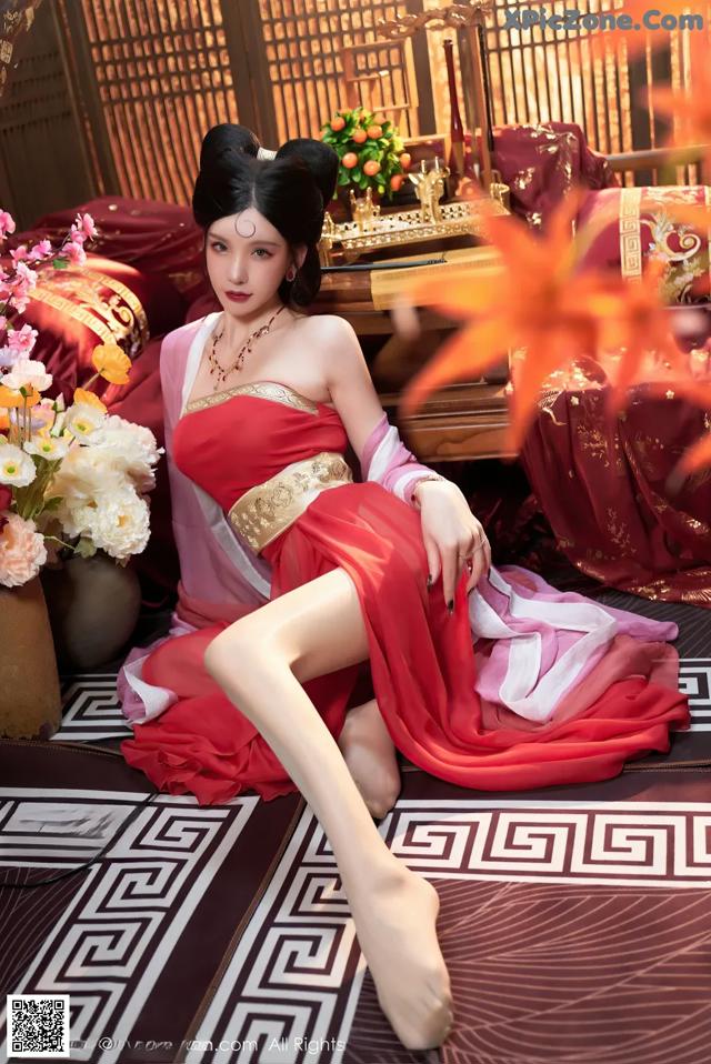 A woman in a red dress sitting on a rug.