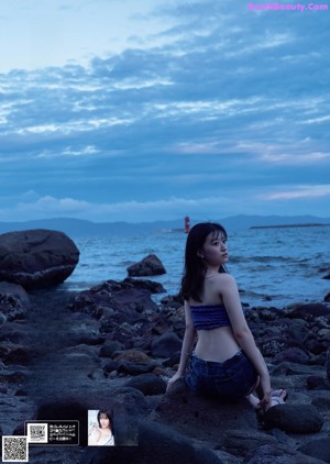 A woman sitting on a rock by the ocean.