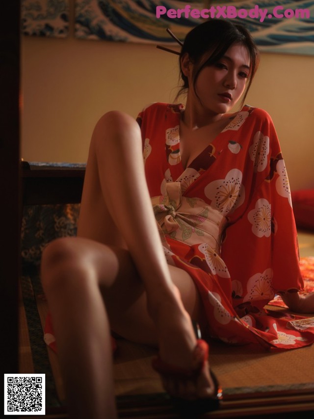 A woman in a red kimono sitting on the floor.