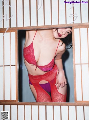 A woman in a red lingerie leaning against a window.