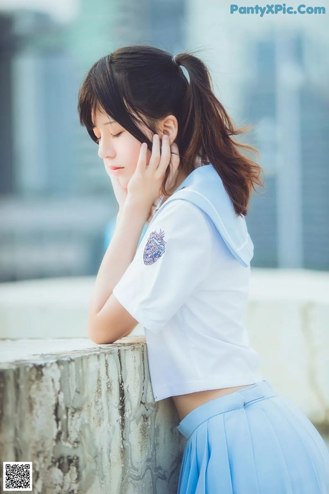A woman in a school uniform leaning against a wall.