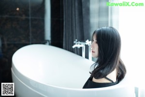 A woman in a black lingerie sitting in a bathtub.