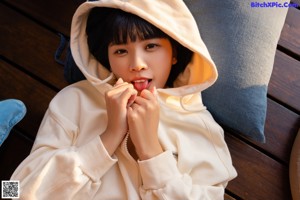 A woman in a white hoodie sitting on a bed.