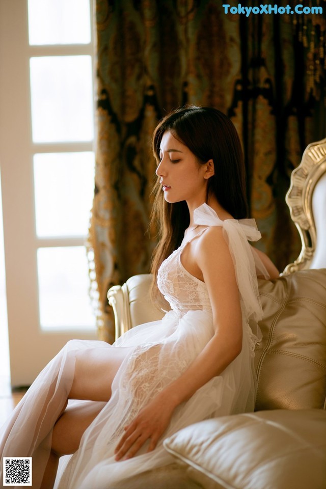 A woman in a white dress sitting on a couch.