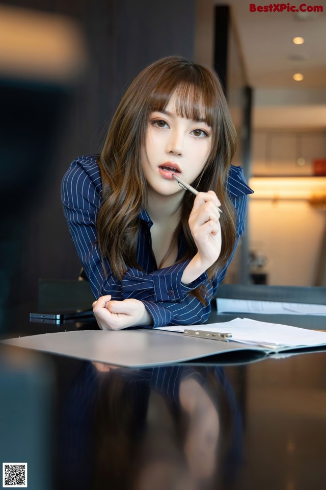 A woman sitting at a table with a pen in her mouth.