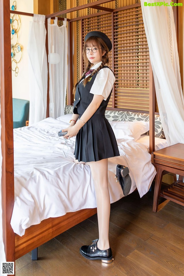 A woman in a black dress and hat standing on a bed.