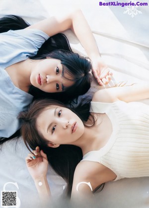 A couple of women laying on top of a bed.