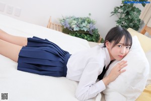 A woman in a school uniform sitting on a bed.