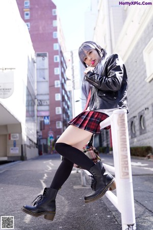 A woman in a black bra top and plaid skirt posing by a window.