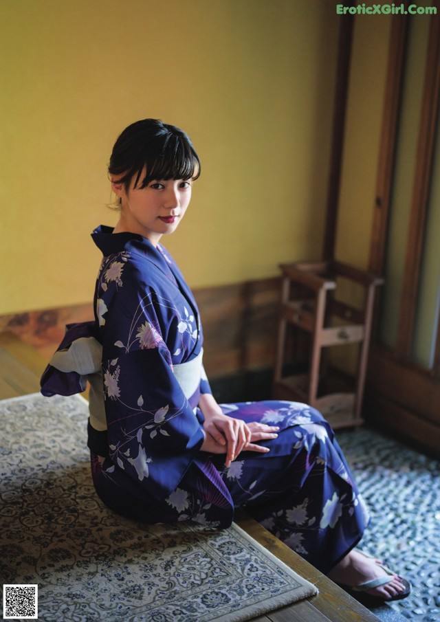 A woman in a blue kimono sitting on a rug.