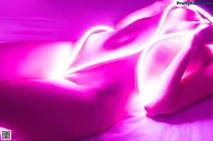 A woman sitting on a bed with a pink light on her back.