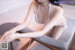 A woman in a white bikini leaning against a wall.