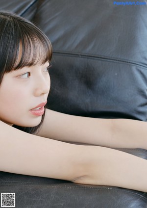 A woman in a yellow and white striped bikini sitting on a black couch.